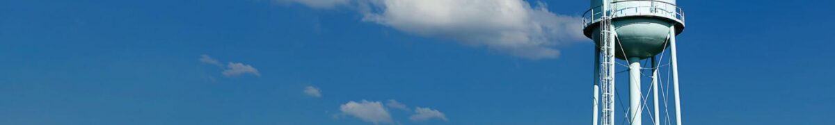 White water tower standing against a bright blue sky with scattered clouds, representing water and wastewater system infrastructure.